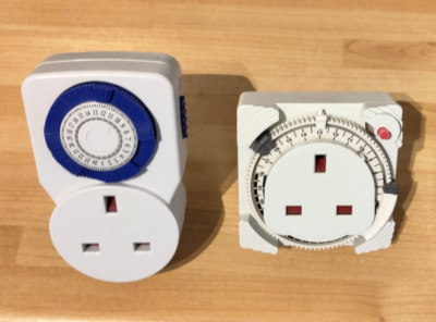 Two mechanical timer plugs with UK sockets. The one on the left has retained switches. The one on the right has a larger ring with removable pegs.