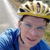 Mugshot of James cycling on a road in the sunshine.